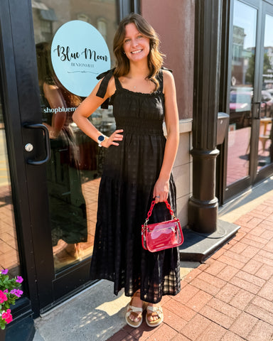 Woman in a black dress with a red handbag standing outside a store named 'Blue Moon'.