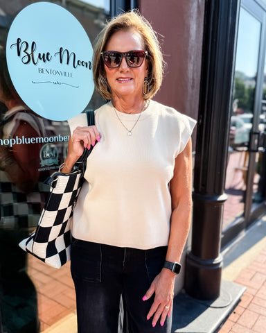Woman holding a checkered bag in front of a store with 'Blue Moon' branding.