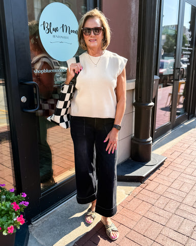 Woman standing outside a store holding a checkered bag, with 'Blue Moon' branding visible.