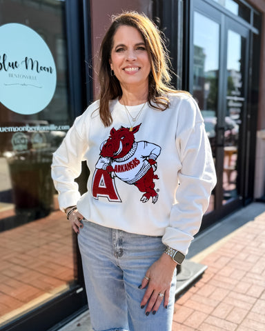 Woman wearing a white sweatshirt with a red and black graphic design, standing in front of a store.