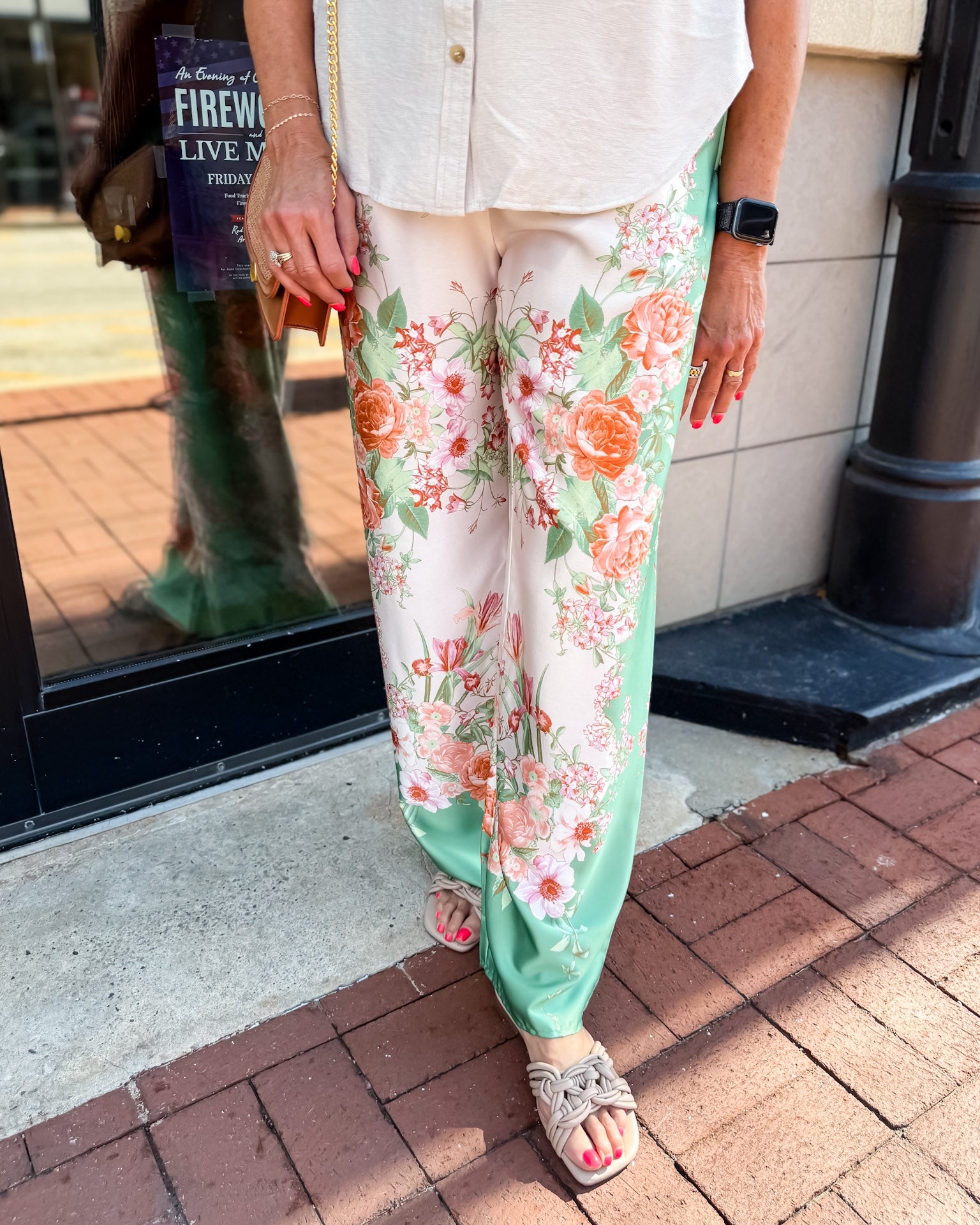 Person wearing floral pants and a white shirt on a sidewalk.