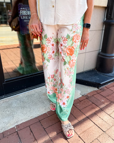 Person wearing floral pants and a white shirt on a sidewalk.