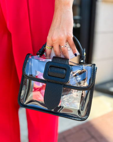 Clear handbag with black strap held by a person wearing a red garment.
