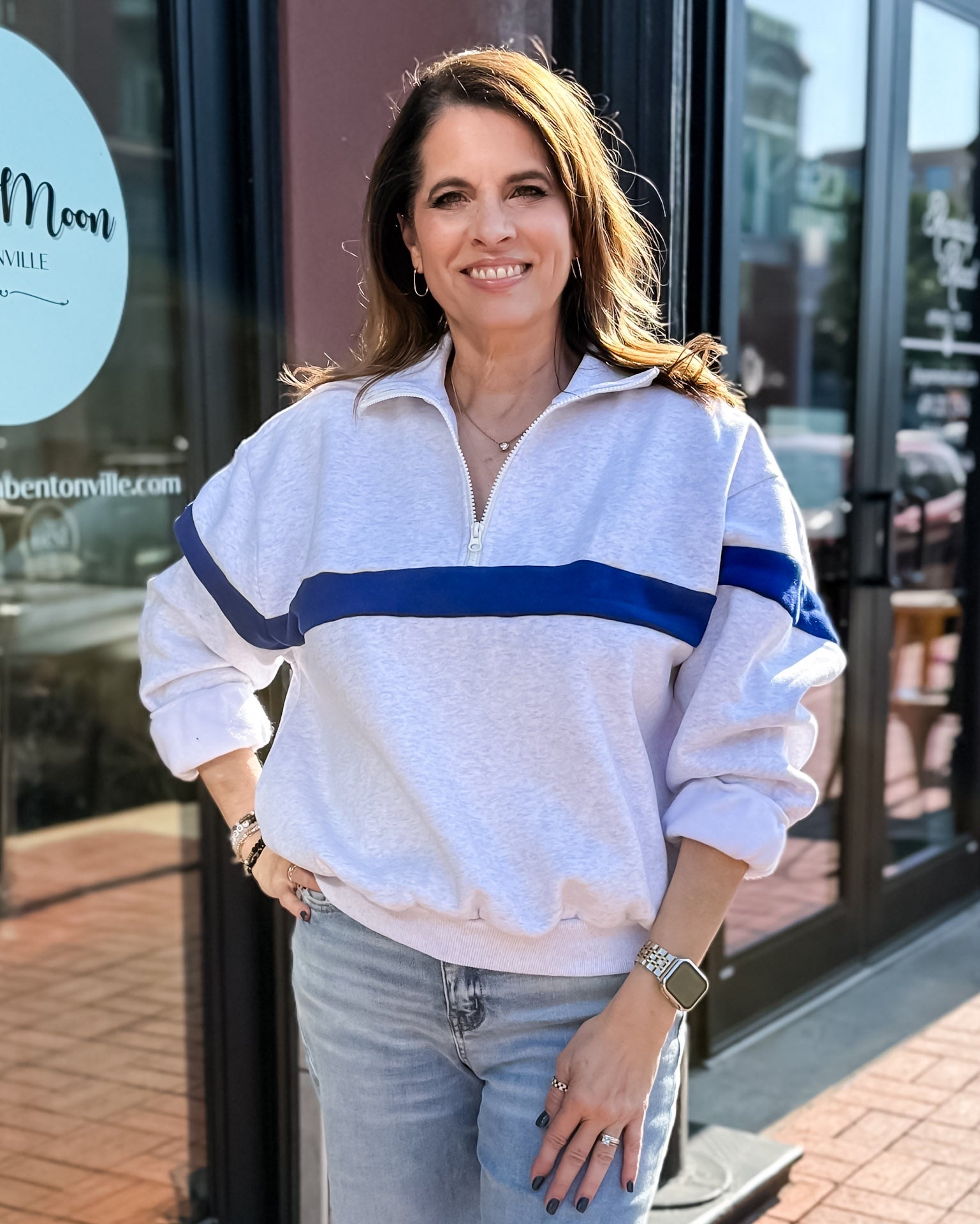 Woman wearing a white sweatshirt with blue stripes and jeans standing in front of a store.