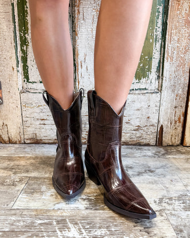 Brown cowboy boots on a wooden floor with a rustic background