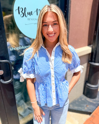 Model wearing a blue and white striped cotton peplum blouse with puff sleeves, bow-tie cuffs, contrast white collar, and button-front closure.