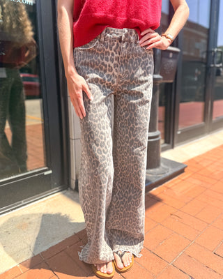 Model wearing faded leopard print high-rise wide leg jeans with a raw hem, five-pocket styling, and a relaxed full-length silhouette paired with a red sweater.