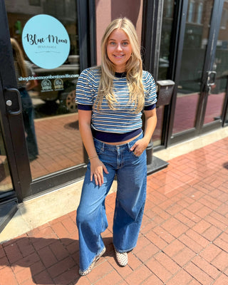  Woman wearing navy, blue, and white striped knit top with wide-leg jeans, standing outside Blue Moon Bentonville storefront 