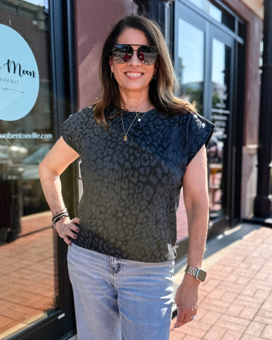 Woman wearing a patterned top and sunglasses standing in front of a store.