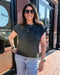 Woman wearing a patterned top and sunglasses standing in front of a store.