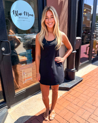 Model wearing a black sleeveless active dress with a twist-back detail and open back design.