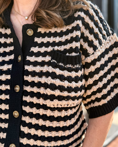Close-up of a person wearing a black and beige striped cardigan with gold buttons.