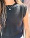 Person wearing a black sleeveless top with a heart-shaped pendant necklace.