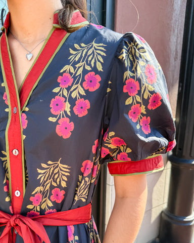 Person wearing a floral dress with red accents, standing against a neutral background.