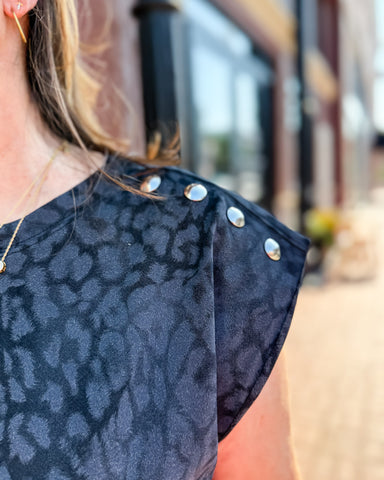 Close-up of a person wearing a dark blue patterned top with silver buttons, blurred background