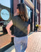 Woman wearing a patterned shirt and jeans standing in front of a store with 'Blue Moon' branding.