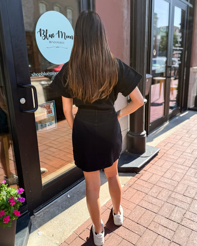 Woman in a black dress standing outside a store with 'Blue Moon' branding.