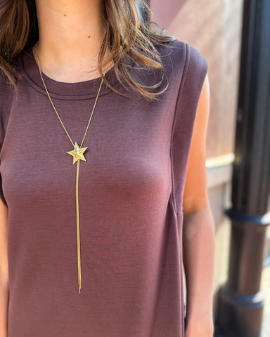 Person wearing a long gold necklace with a star pendant on a blurred background