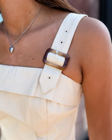 Close-up of a beige strap with a large brown buckle on a person wearing a light-colored top.