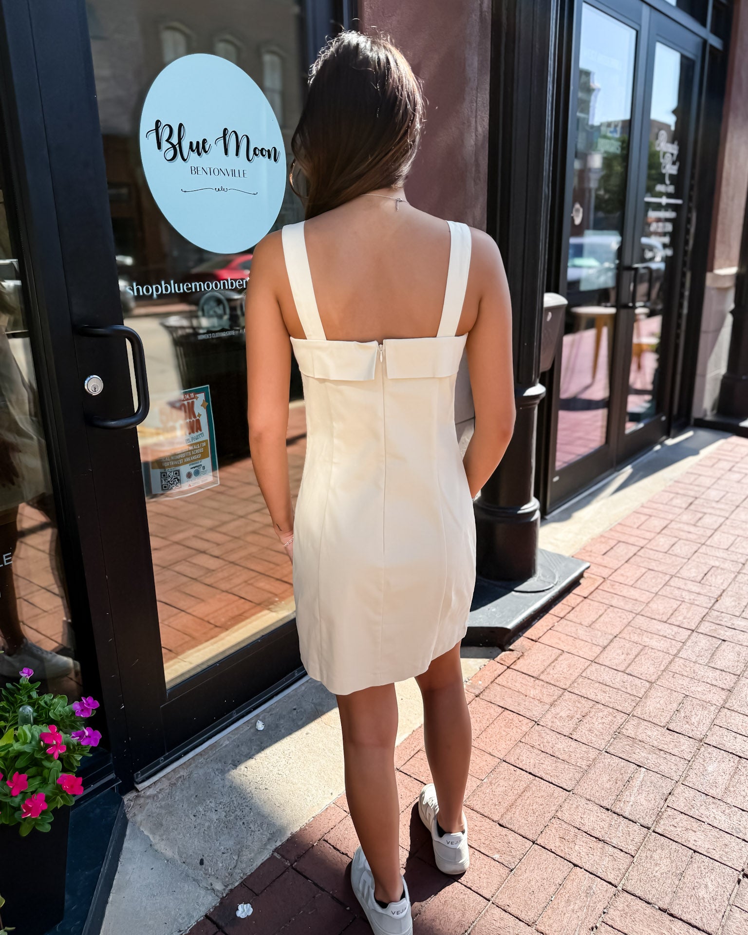 Woman in a white dress standing outside a store with 'Blue Moon' branding.
