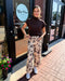 Woman standing outside a store named 'Blue Moon' wearing a brown top and floral pants.