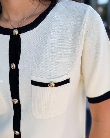 Close-up of a white shirt with black trim and gold buttons.