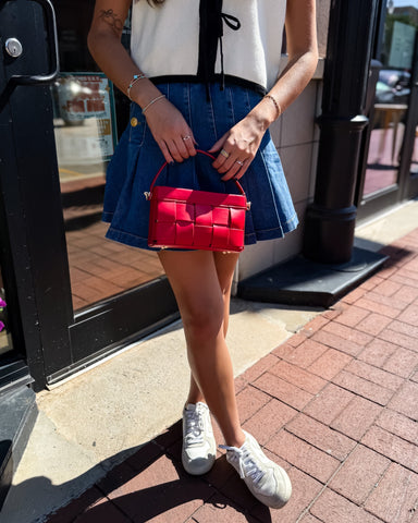 Person holding a red handbag on a sidewalk