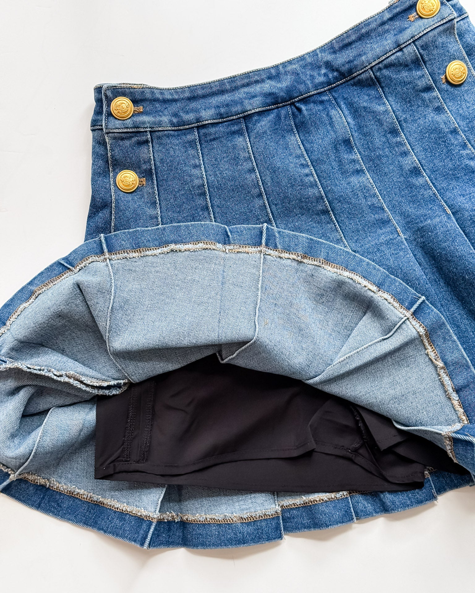 Close-up of a blue denim skirt with yellow buttons on a white background