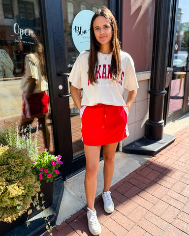 Woman wearing a white t-shirt with red text and a red skirt standing outside a store.