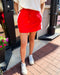 Person wearing red shorts and white sneakers standing on a sidewalk.