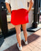 Person wearing a red skirt and white sneakers on a sidewalk.