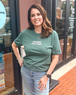 Model wearing a green Love God Love People Christian graphic t-shirt with inspirational front and back faith-based artwork.