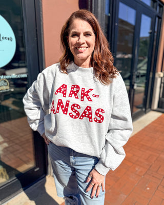 Model wearing a grey mockneck sweatshirt with red, white-star-filled Arkansas lettering, styled with light-wash jeans
