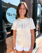 Woman wearing a 'Good is Good' t-shirt in front of a store with a Blue Moon Bendon Hills sign.