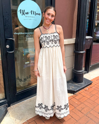 Model wearing an ivory embroidered scallop trim maxi dress with black contrast embroidery and adjustable spaghetti straps.