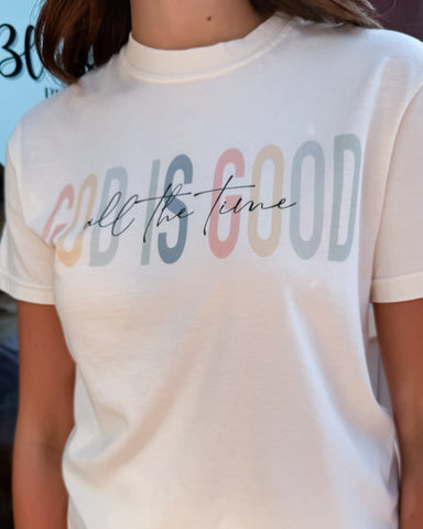 White t-shirt with colorful text 'God is good all the time' worn by a person.