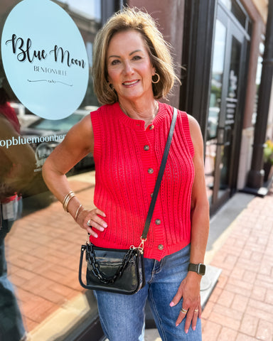 Woman in a red sleeveless sweater and blue jeans holding a black handbag, with 'Blue Moon' branding in the background.