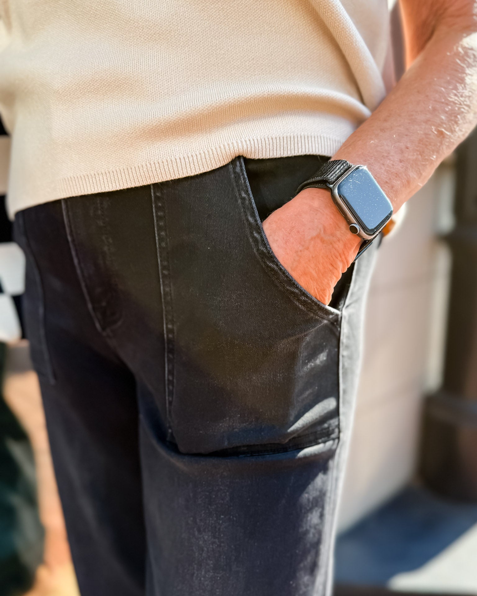 Person wearing a beige sweater and black pants with a watch on a blurred background