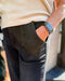 Person wearing a beige sweater and black pants with a watch on a blurred background