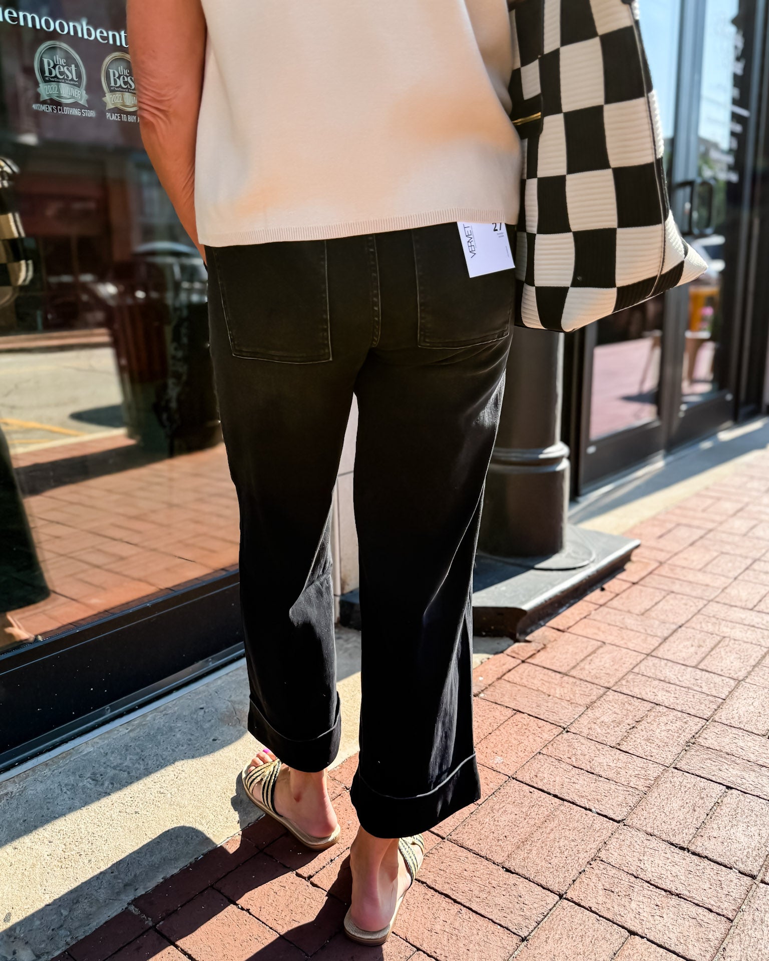 Person wearing black pants and a checkered jacket on a sidewalk.