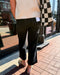 Person wearing black pants and a checkered jacket on a sidewalk.