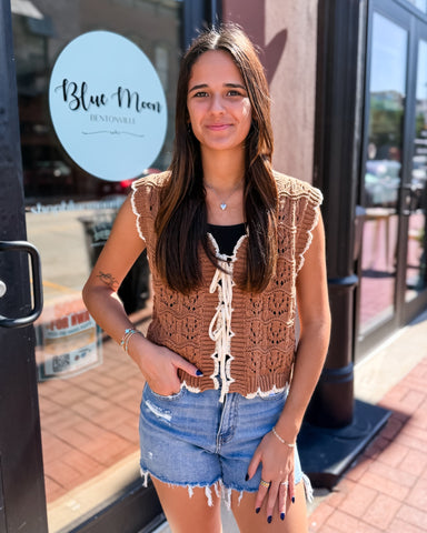 Woman wearing a brown crochet vest and denim shorts standing in front of a store with 'Blue Moon' sign.