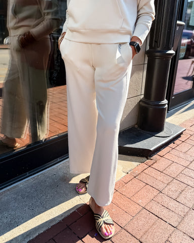 Person wearing a beige outfit standing on a sidewalk next to a storefront window.