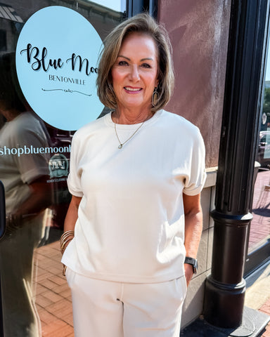 Woman in a white outfit standing outside a building with 'Blue Moon Bentonville' sign.