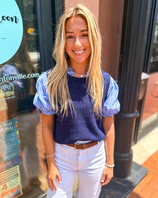 Model wearing a navy layered sweater vest top with blue and white striped puff sleeves and a textured knit body.