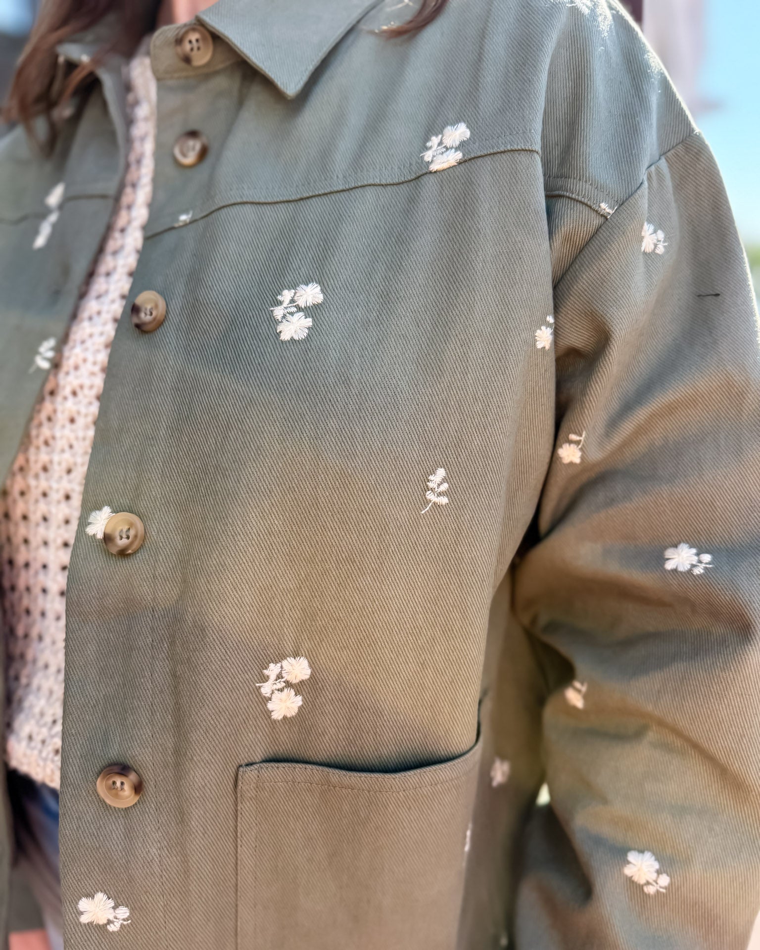 Green jacket with floral patterns and buttons on a blurred background