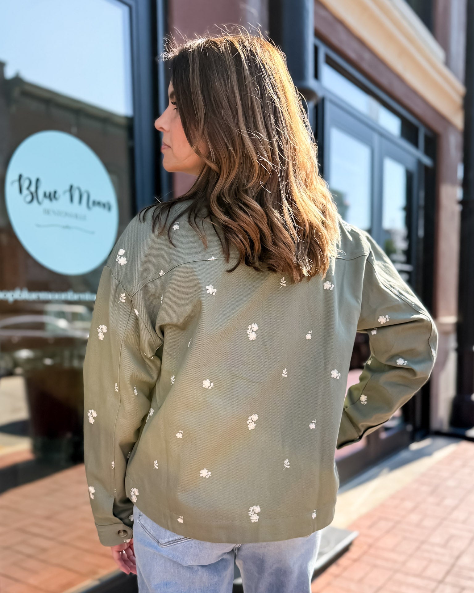Woman wearing a light green jacket with white floral patterns standing on a sidewalk.