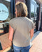 Person wearing a beige top and blue jeans standing outside a building with a glass door.