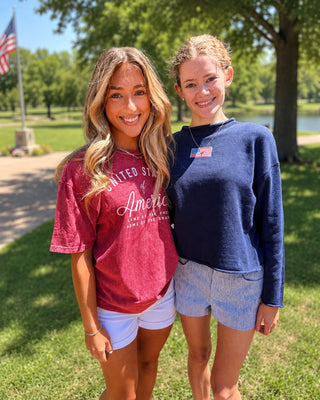 Two women standing outdoors in a park, wearing 'United States of America' t-shirts.