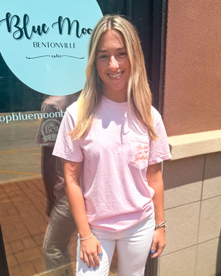 Model wearing a light pink Comfort Colors graphic T-shirt with a front pocket design and large coral "The Lord Is My Shepherd" graphic on the back, paired with white jeans.